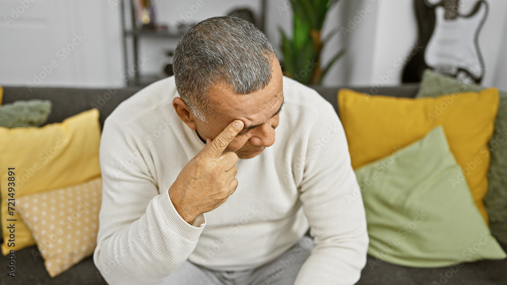 Pensive hispanic man thinking indoors, touching face while sitting on a couch, home interior background. Pensive hispanic man thinking indoors, touching face while sitting on a couch, home interior background.