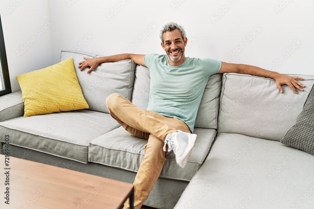 Middle age grey-haired man smiling confident sitting on sofa at home