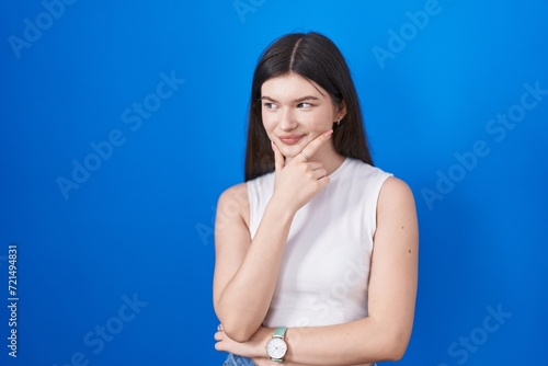 Young caucasian woman standing over blue background looking confident at the camera smiling with crossed arms and hand raised on chin. thinking positive. © Krakenimages.com