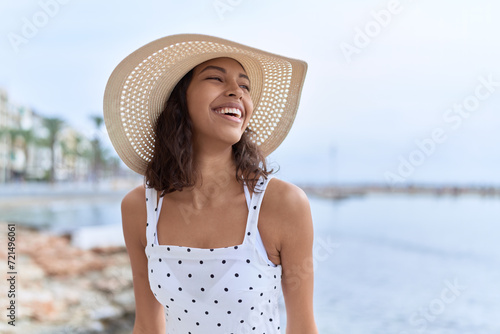 Young african american woman wearing summer hat looking to the side at seaside