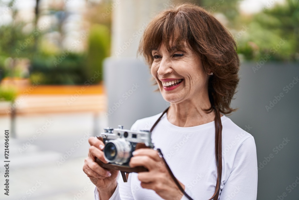 Middle age woman smiling confident using vintage camera at street