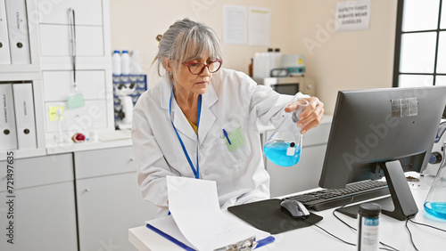 Mature woman scientist analyzing chemicals in a laboratory setting  with computer and lab equipment.