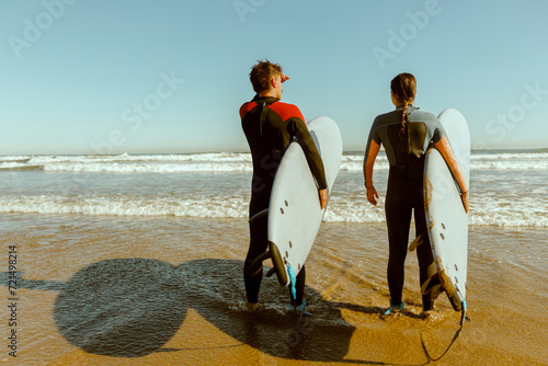 Back view of surfers with surfboards entering towards ocean for surfing on waves