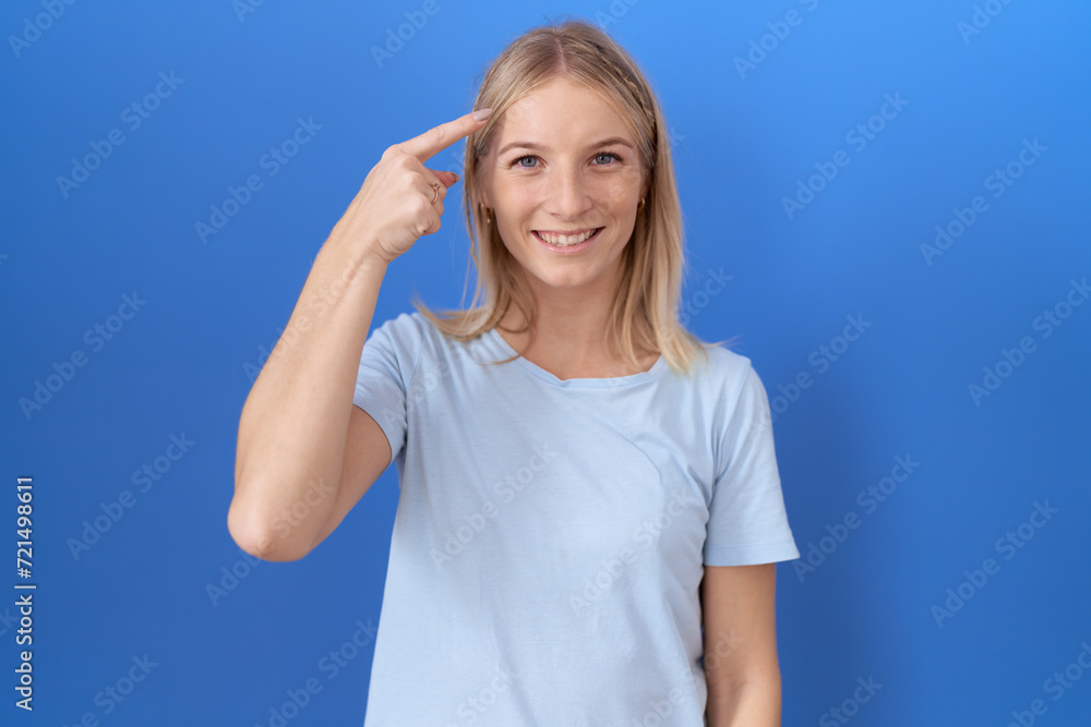 Young caucasian woman wearing casual blue t shirt smiling pointing to head with one finger, great idea or thought, good memory Young caucasian woman wearing casual blue t shirt smiling pointing to head with one finger, great idea or thought, good memory