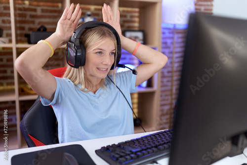 Young caucasian woman playing video games wearing headphones doing bunny ears gesture with hands palms looking cynical and skeptical. easter rabbit concept. photo