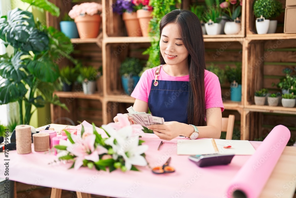Young chinese woman florist smiling confident counting dollars at flower shop