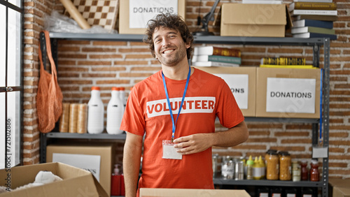 Young hispanic man volunteer smiling confident standing by donations cardboard box at charity center photo