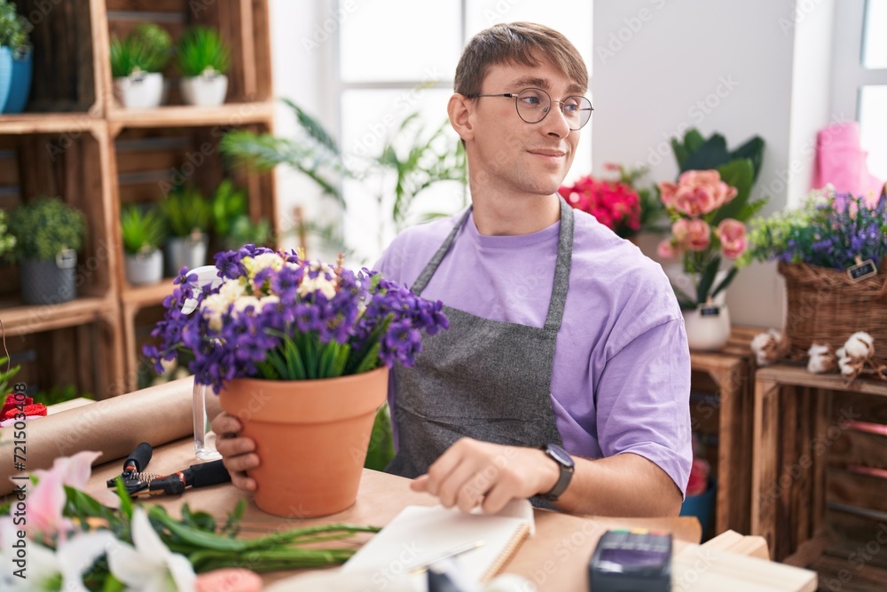 Caucasian blond man working at florist shop looking away to side with smile on face, natural expression. laughing confident.