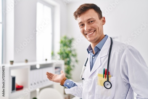 Young man doctor smiling confident standing with welcome gesture at clinic