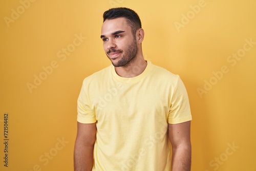 Young hispanic man standing over yellow background smiling looking to the side and staring away thinking.