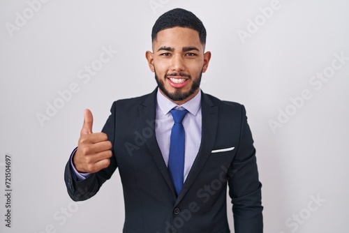 Young hispanic man wearing business suit and tie doing happy thumbs up gesture with hand. approving expression looking at the camera showing success.