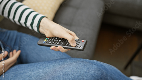 Close-up of a woman reclining on a sofa at home, pressing a button on a tv remote control.