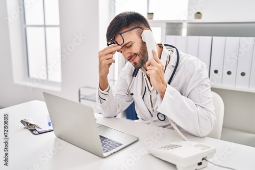 Young hispanic man doctor talking on telephone stressed at clinic