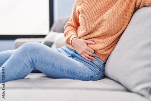Young beautiful hispanic woman suffering for stomach ache sitting on sofa at home