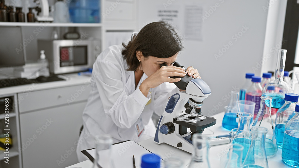 Young beautiful hispanic woman scientist using microscope at laboratory Young beautiful hispanic woman scientist using microscope at laboratory
