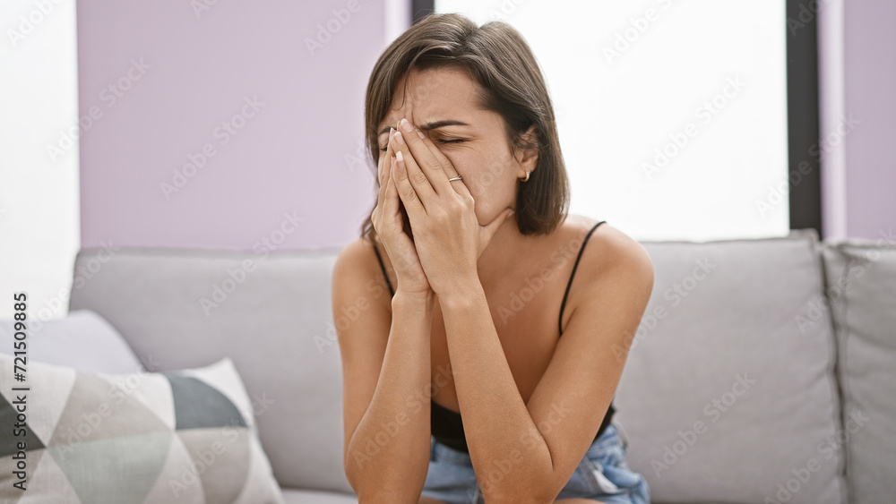 Emotional portrait, young, beautiful hispanic woman, with short hairstyle, sitting on home's interior sofa, crying; an image of stress, unhappiness, mental suffering, and tiredness. Emotional portrait, young, beautiful hispanic woman, with short hairstyle, sitting on home's interior sofa, crying; an image of stress, unhappiness, mental suffering, and tiredness.