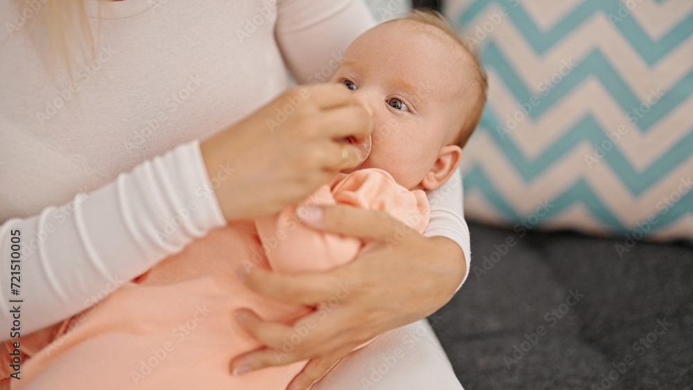 Mother and daughter sitting on sofa sucking pacifier at home Mother and daughter sitting on sofa sucking pacifier at home