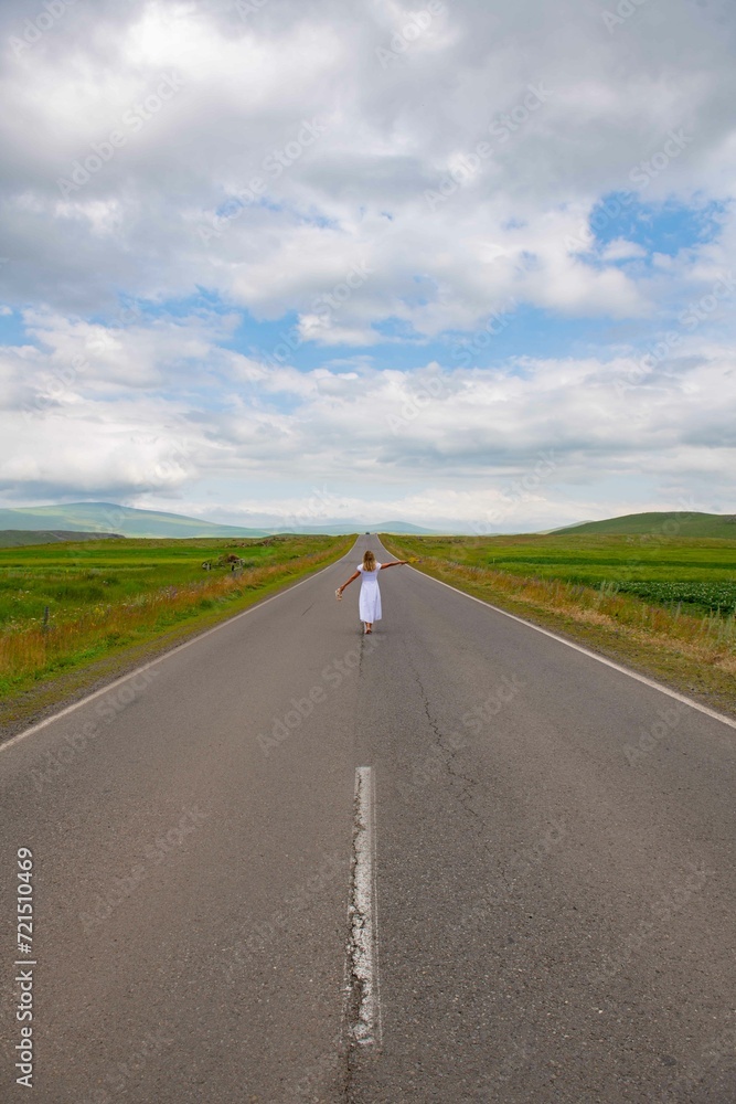 A girl in a white dress is walking along a picturesque road