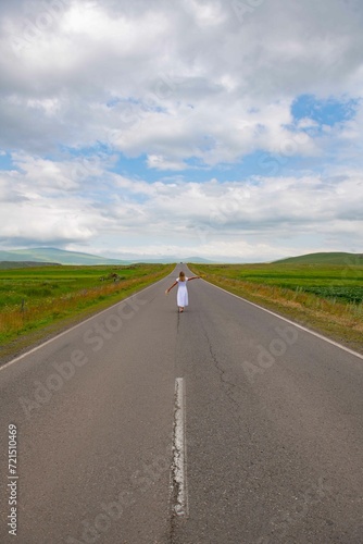 A girl in a white dress is walking along a picturesque road