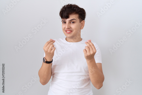 Young non binary man wearing casual white t shirt doing money gesture with hands, asking for salary payment, millionaire business photo