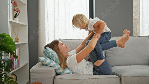 Confident caucasian mother and daughter lying comfortably on a sofa, playing and smiling in the warmth of their home