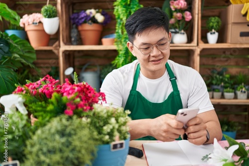 Young chinese man florist smiling confident using smartphone at flower shop