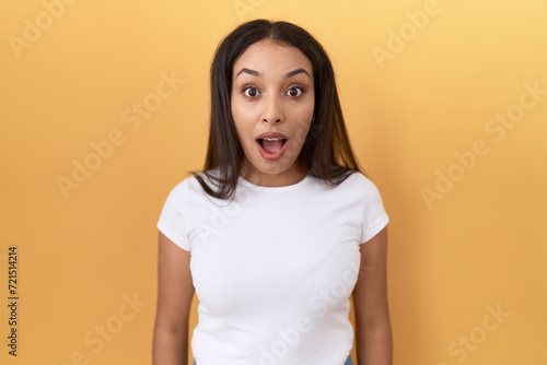 Young arab woman wearing casual white t shirt over yellow background afraid and shocked with surprise and amazed expression, fear and excited face.