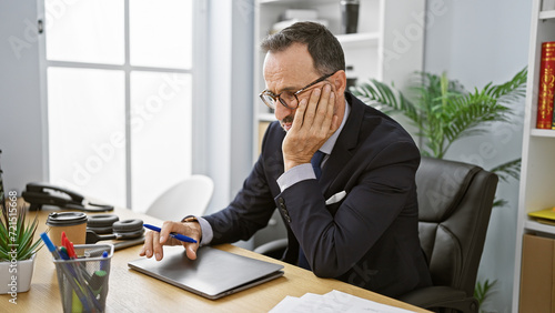 Cuadro en lienzo Worried middle age man with grey hair at work, a worried, grey-haired businessman sitting at his office desk, wrestling with doubts