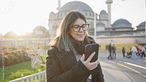 Smiling woman using smartphone at taksim square with taksim mosque in background at sunset, istanbul, turkey. photo