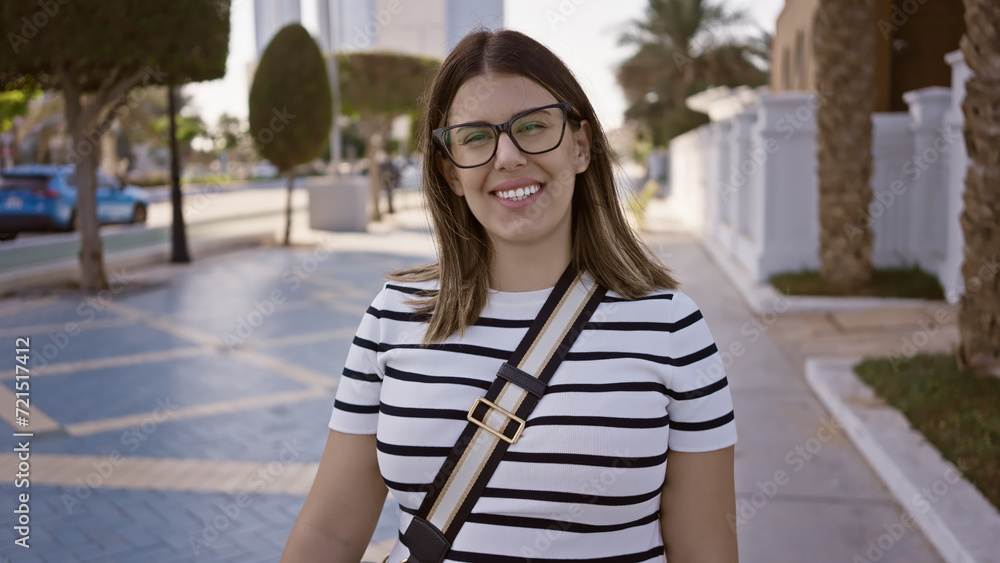 Smiling woman with glasses posing in a modern abu dhabi city street, showcasing urban life and travel.