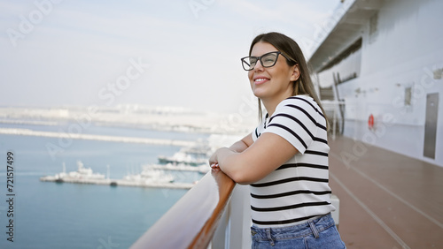 Smiling woman leaning on the railing of a cruise ship deck against an ocean backdrop.