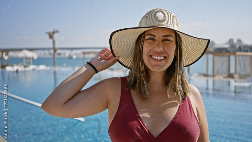 Smiling woman wearing swimsuit and sunhat at a luxurious poolside with a sea view