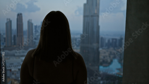 Silhouetted woman observing a blurred cityscape from an observatory high above the urban skyline