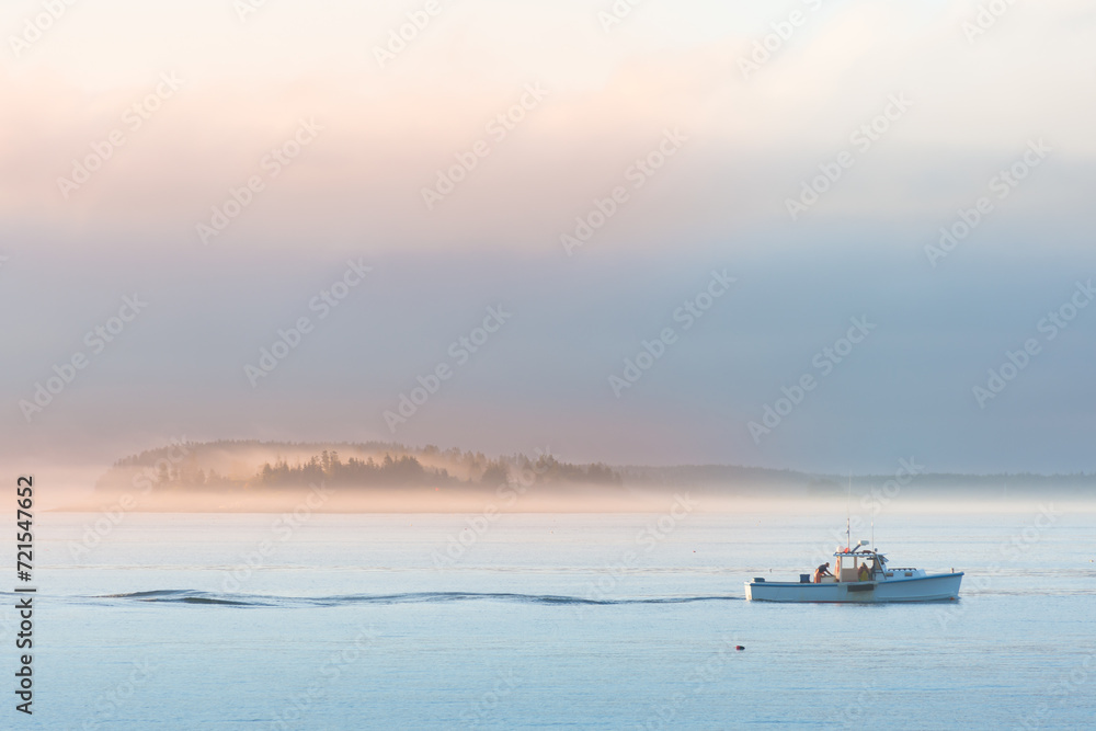 Lobster boat setting traps at sunrise along the coast of Maine. Fog covered islands in distance reflecting rising sun.