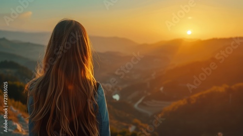 Side view of female traveler with long wavy hair standing on viewpoint and observing picturesque landscape with mountains under sunset sky © buraratn