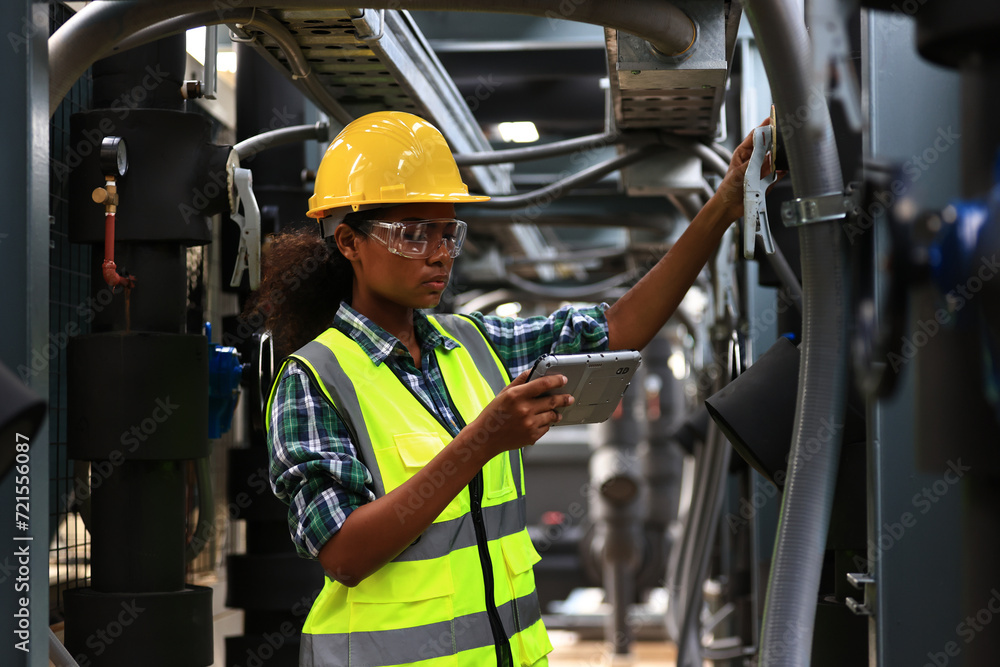 Female engineer wearing a yellow safety vest and yellow helmet  working check Industry cooling system, HVAC of large industrial building  - obrazy, fototapety, plakaty 