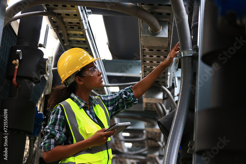 Female engineer wearing a yellow safety vest and yellow helmet  working check Industry cooling system, HVAC of large industrial building  photo