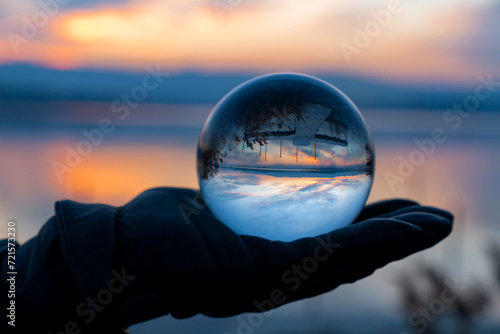 View of nature through a glass ball, summer sunset time. hand holding crystal glass ball against nature background with reflections © FATIR29