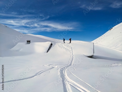 Freeriders ride over a snow covered house roof. Skiers go up to the roof of an alpine hut and back down again. Freeriding in Glarus Switzerland ​. High quality photo
