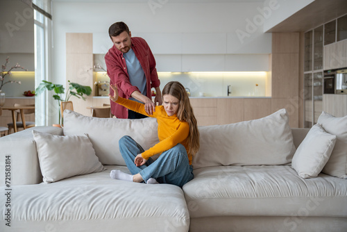 Unhappy helpless abused wife sitting on sofa with depressed face expression and angry annoyed nervous husband touching woman hand rudely. Jealousy, quarrels, conflicts, marital problems in family life photo