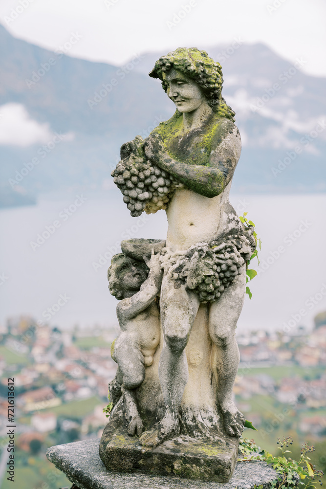 Antique statue of the ancient Greek god Dionysus with a bunch of grapes with a small faun with a bowl in the garden