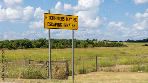 Fotografija Hitchhikers may be escaping inmates sign beside a chainlink fence with barbed wi