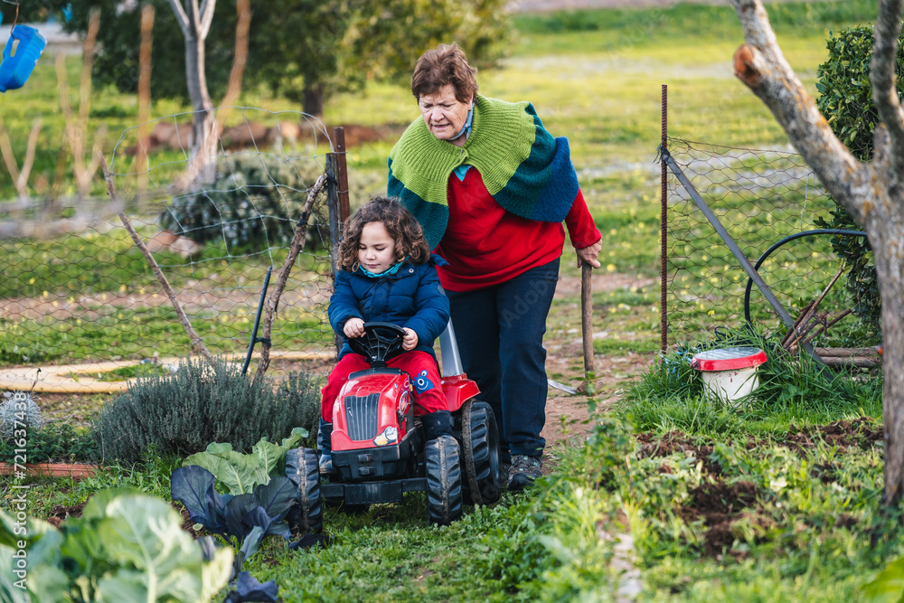 grandmother and grandson playing riding a toy tractor entering the home garden grandmother and grandson playing riding a toy tractor entering the home garden