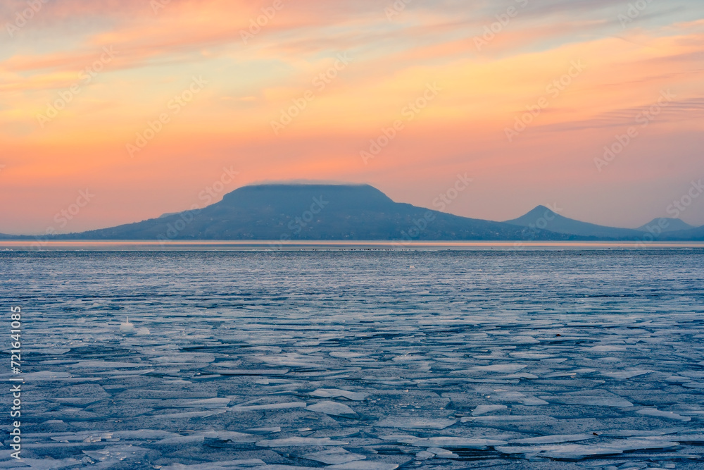 Fonyod, Hungary - Beautiful icebergs on the shore of the frozen Balaton. Badacsony and Gulacs with a spectacular cloudy sunset in the background. Winter landscape.