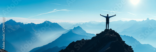 Panorama of young successful man hiker silhouette open arms on mountain peak photo