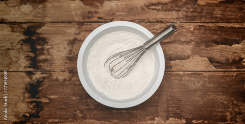 Flour and whisk in a mixing bowl on rustic wood photo