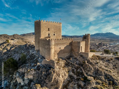 Aerial view of Jumilla medieval castle in Murcia Spain, on a hilltop, imposing irregular shape keep with four floors, crenelated battlements cloudy blue sky background photo