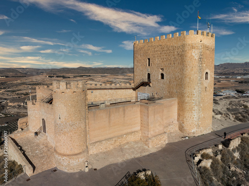 Aerial view of Jumilla medieval castle in Murcia Spain, on a hilltop, imposing irregular shape keep with four floors, crenelated battlements cloudy blue sky background photo
