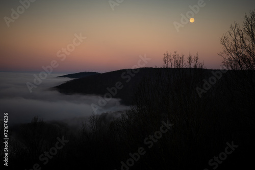 Colorful twilight hour with the moon in view as seen from the bluffs of Sewanee, Tennessee as fog permeates the valley. photo