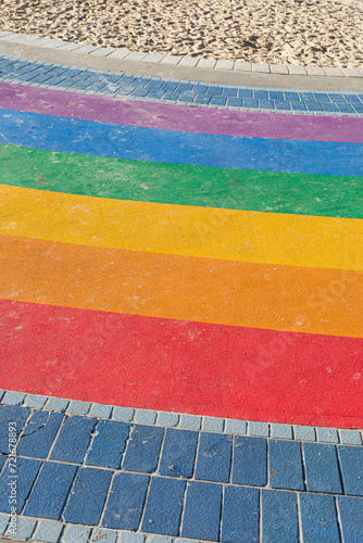 Rainbow-painted floor celebrating LGBT Pride on a beach on a sunny day with sand at the top (ID: 721678893)